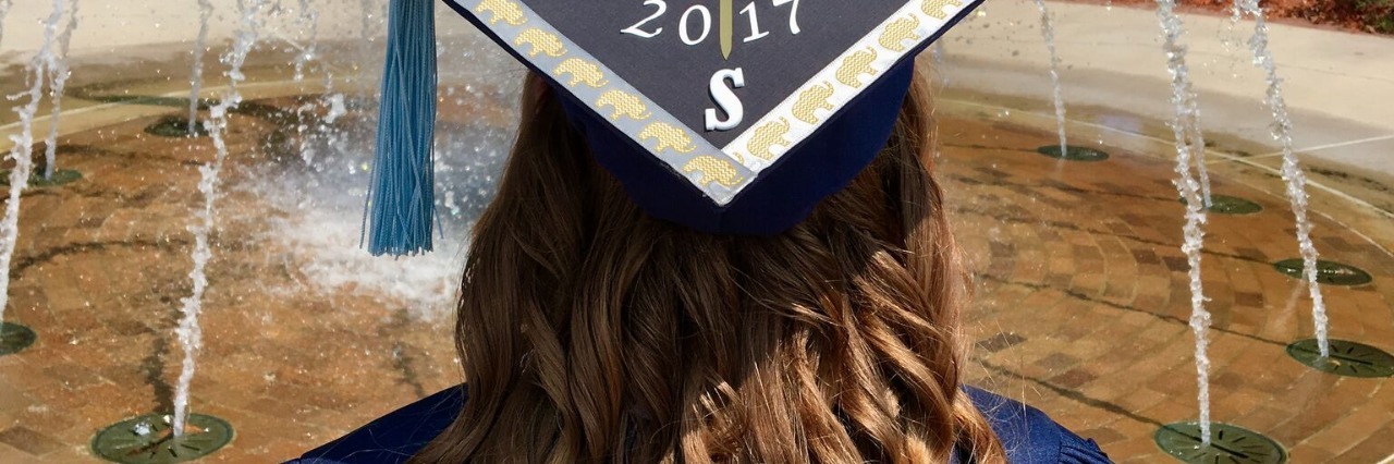 Graduating From College With a Chronic Illness college graduate standing in front of a fountain wearing her cap and gown