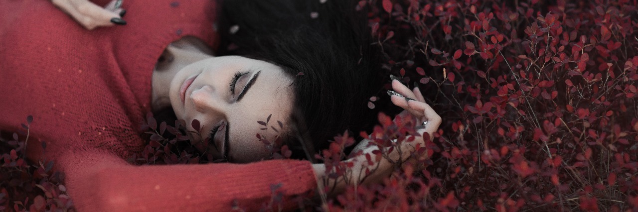 young woman lying in bush with small red leaves wearing red sweater