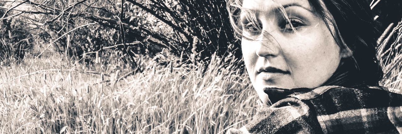 When People Invalidate You Because of Your Bipolar Disorder black and white image of woman in checkered shirt sitting in field looking at camera straight-faced