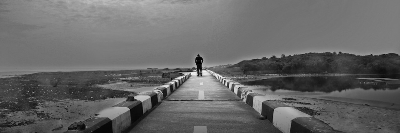 black and white photo of a person walking down a long road