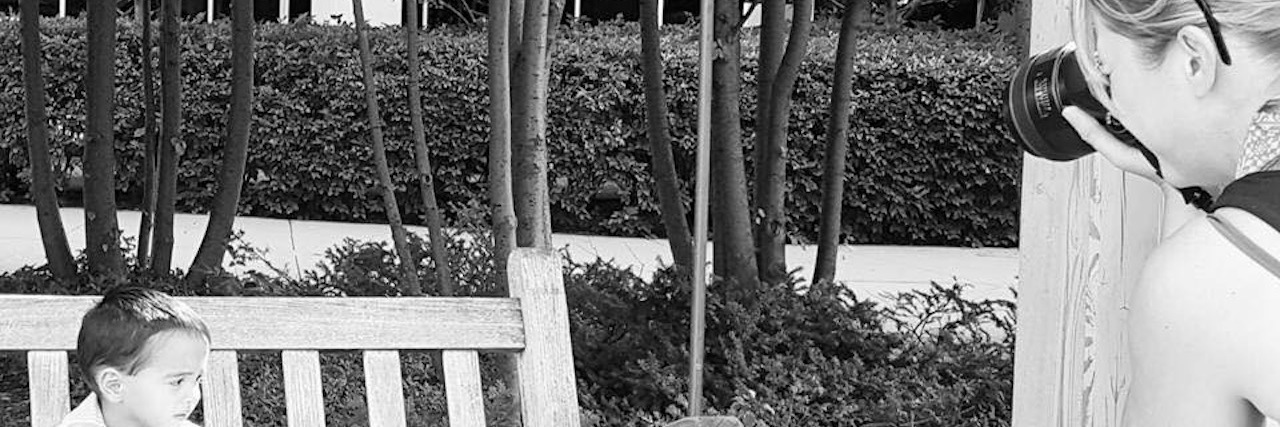 Black and white photo of photographer taking picture of a child with autism sitting on a swing bench