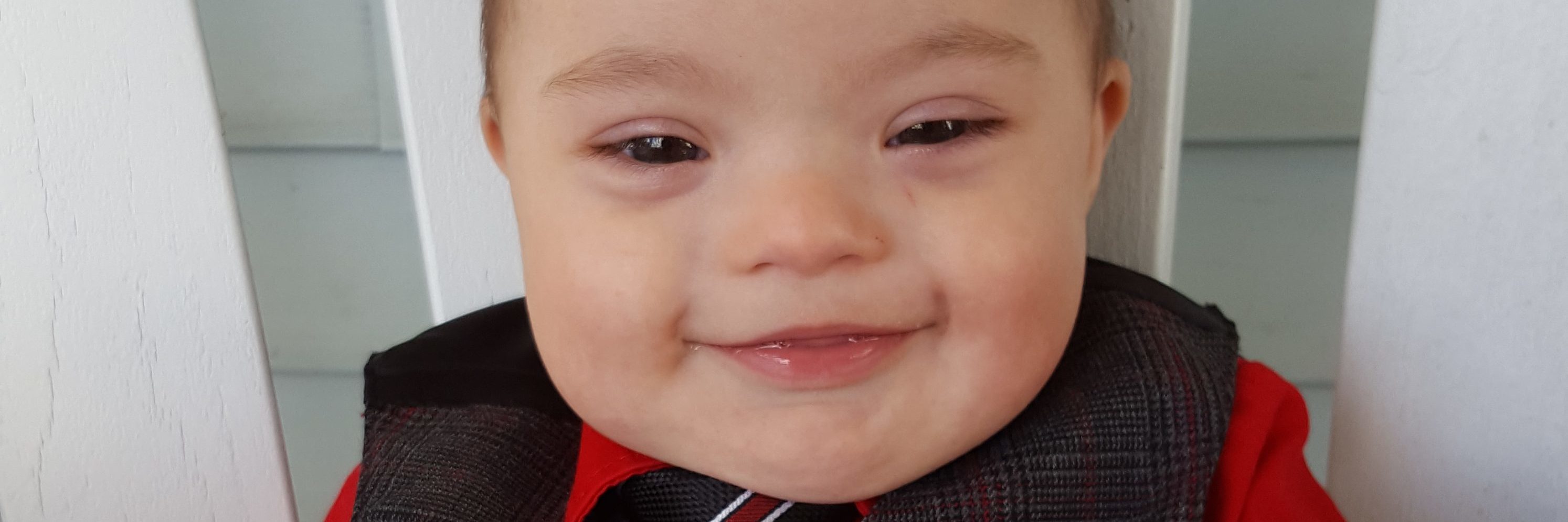The Day a Stranger Recognized My Son Has Down Syndrome Little baby boy with Down syndrome smiling, his thicj dark hair is styled sticking up like a Mohawk and he is wearing a suit with a red shirt