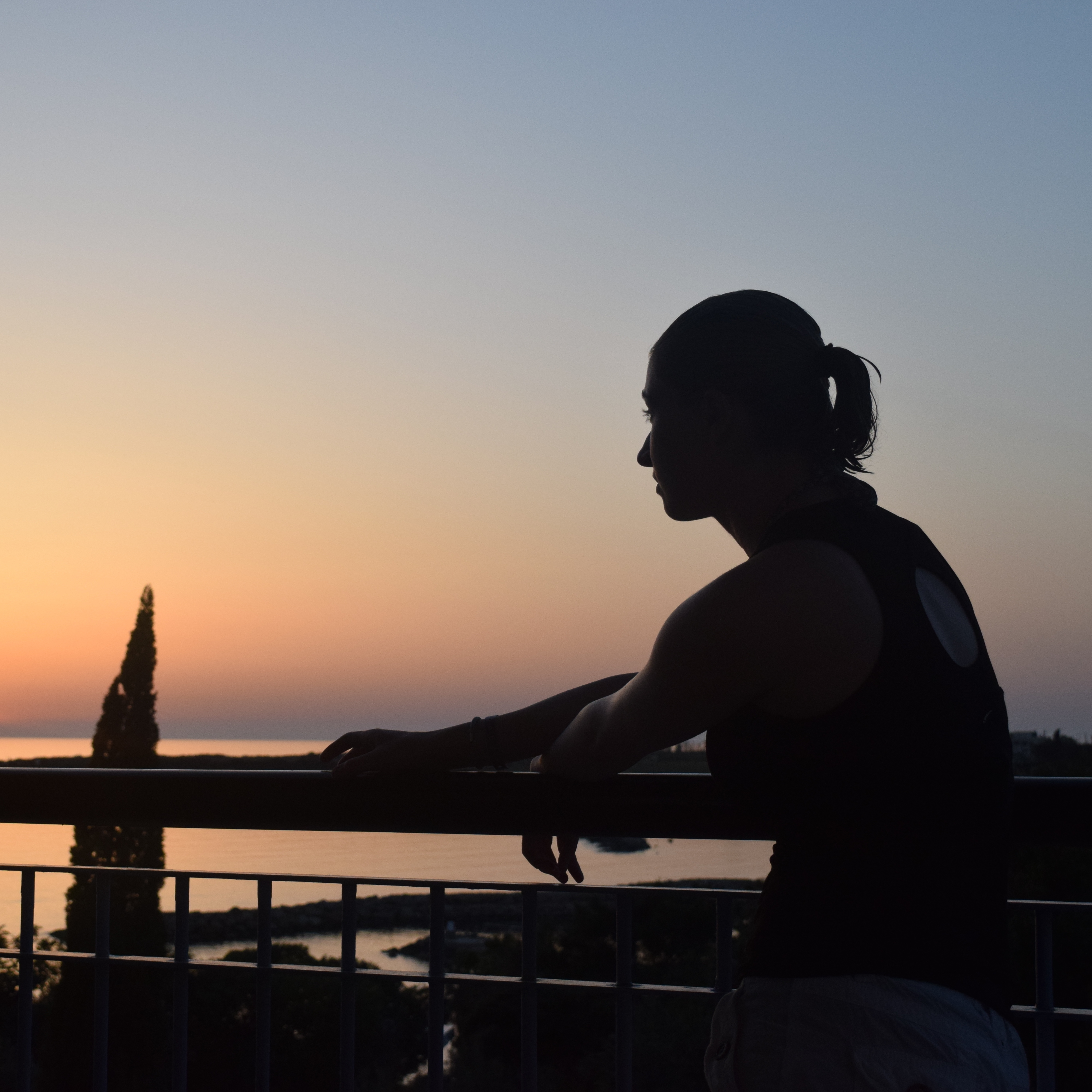 silhouette of a woman standing on a balcony overlooking a lake at sunset