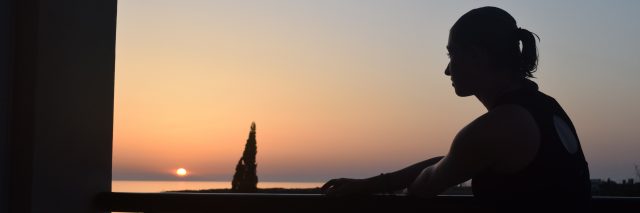 silhouette of a woman standing on a balcony overlooking a lake at sunset