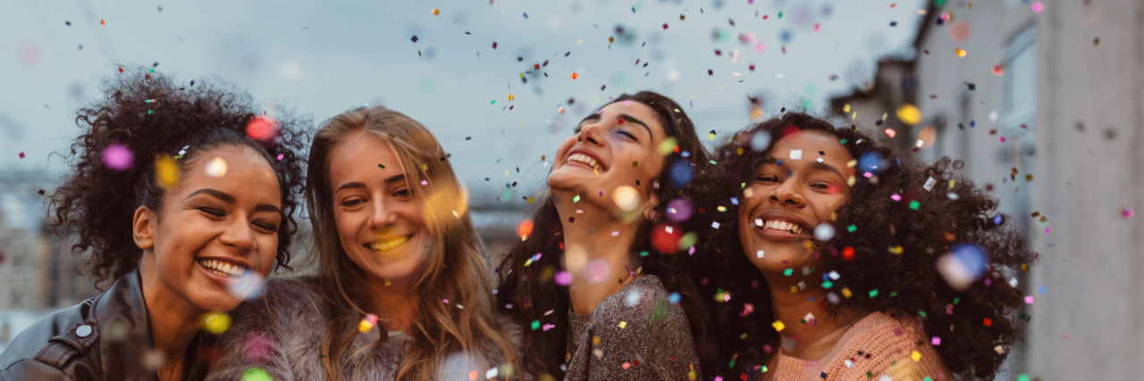 Four beautiful women standing at a terrace under confetti.