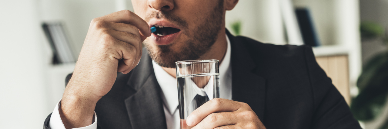 The Biggest Mistake I Made in Taking Medication for My Mental Health businessman taking medication in office in front of laptop