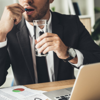 businessman taking medication in office in front of laptop