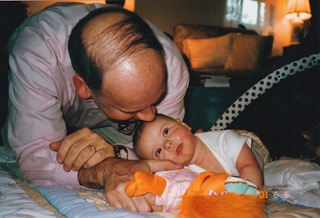 Father leaning over next to baby lying on blanket on floor with stuffed animal