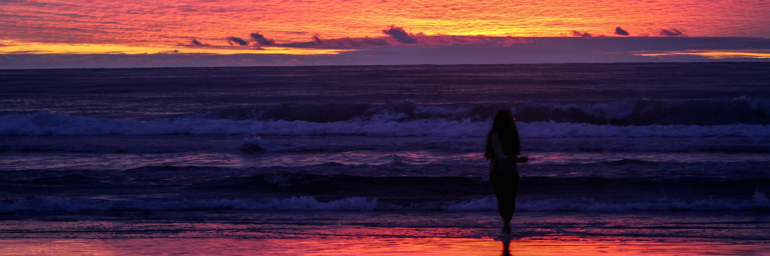 Woman standing on beach near the water at sunset