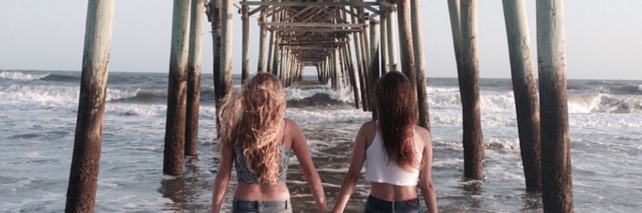 two sisters holding hands under a pier at the beach