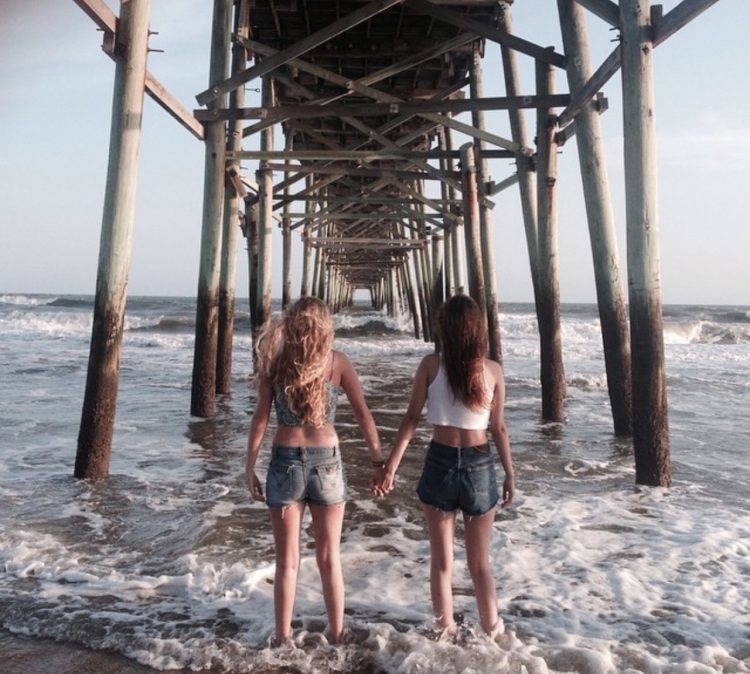 two sisters holding hands under a pier at the beach