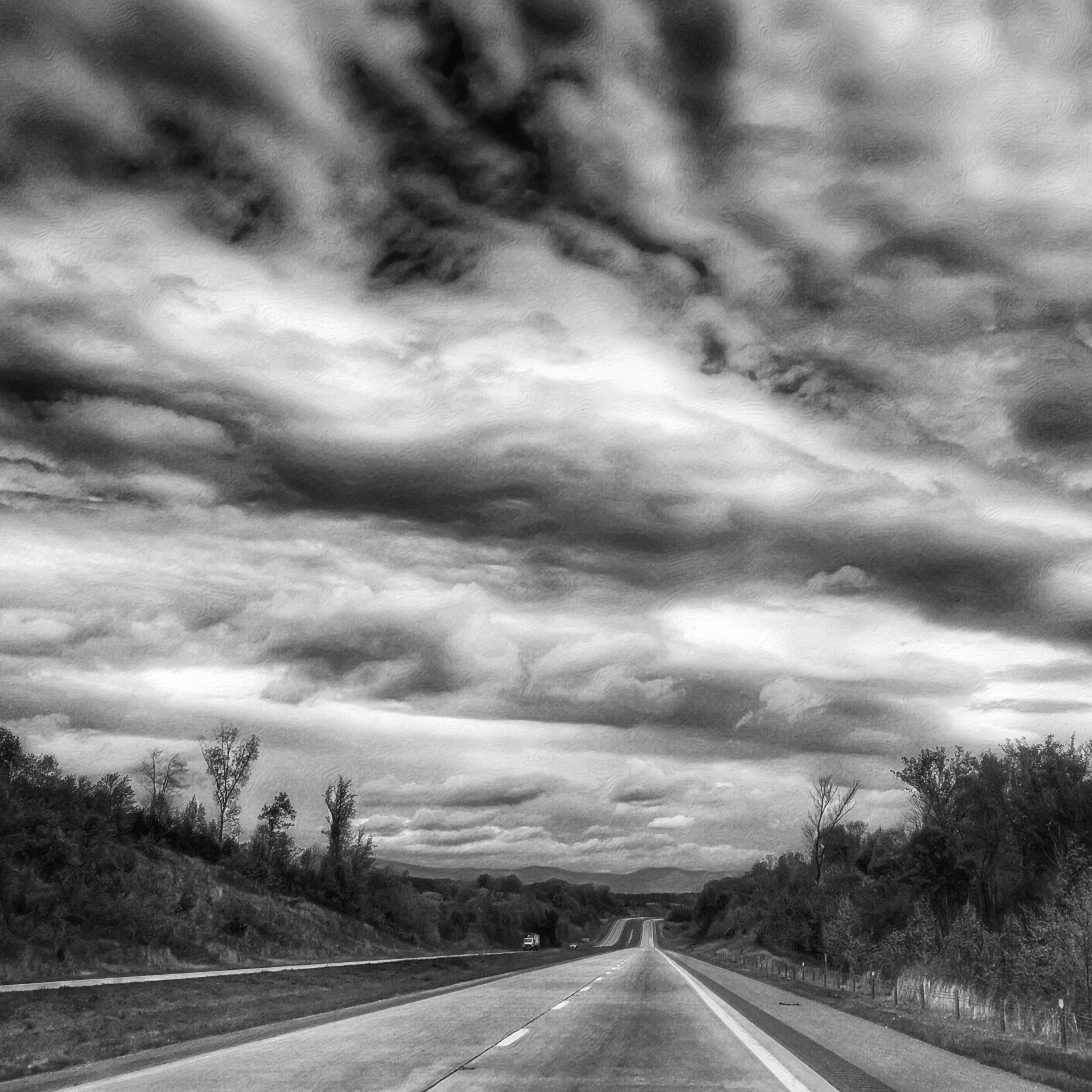 A black and white picture of an empty road on a cloudy day.