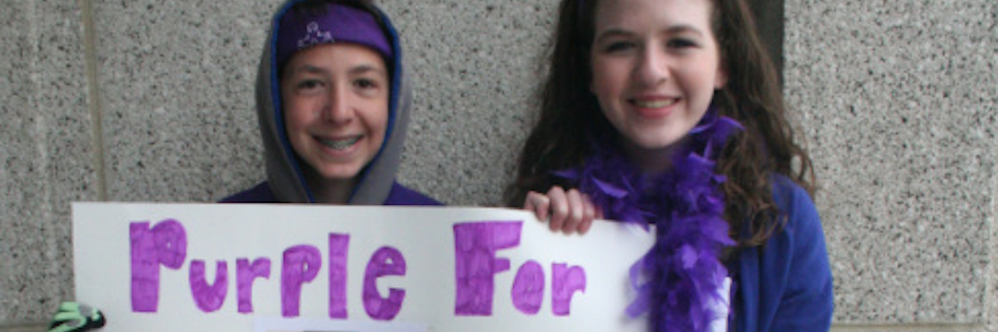 Two people holding a handmade sign that says "Purple for Paul" with a photo and purple ribbons