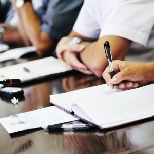 People with arms resting on table, papers and notebooks in front of them, having a meeting