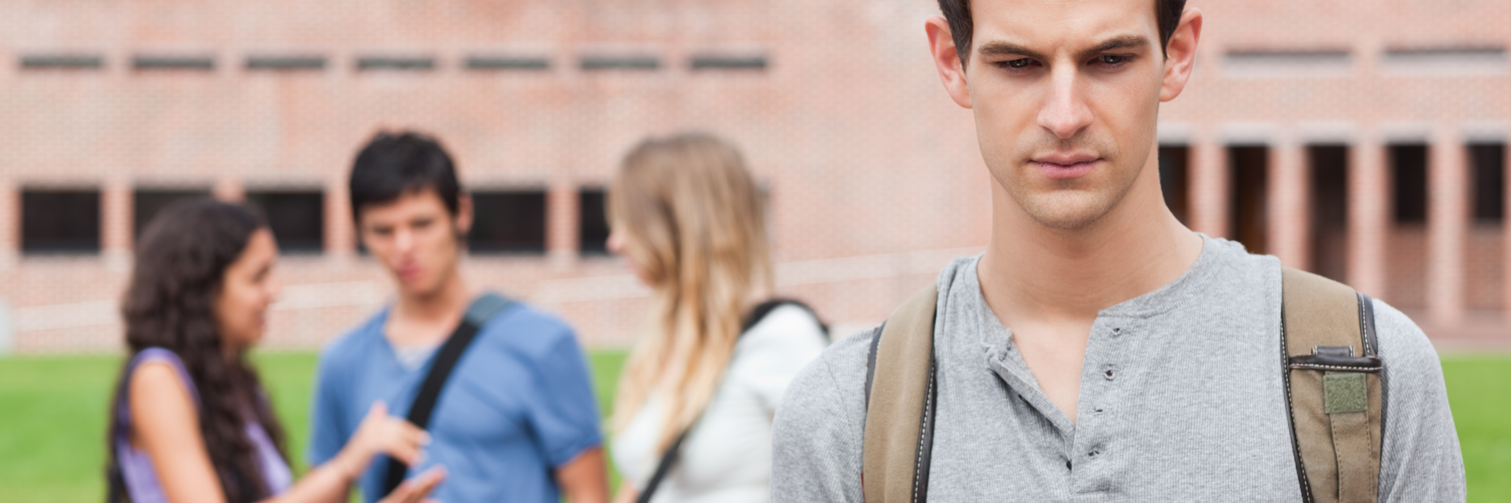 How Overhearing Hurtful Comments About Mental Illness Can Affect You lonely male student standing with group of students gossiping behind him