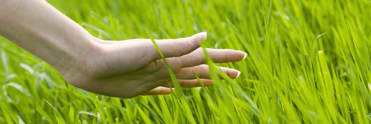 15 Grounding Exercises to Manage Stress From Anxiety or Trauma woman's hand touching the grass, 'feeling nature'