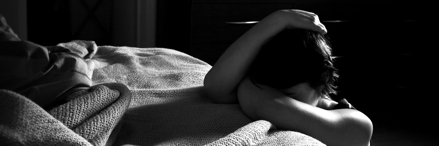 Phoning My Psychiatrist Saved My Life When I Was Suicidal woman kneeling on floor next to bed leaning on bed crying