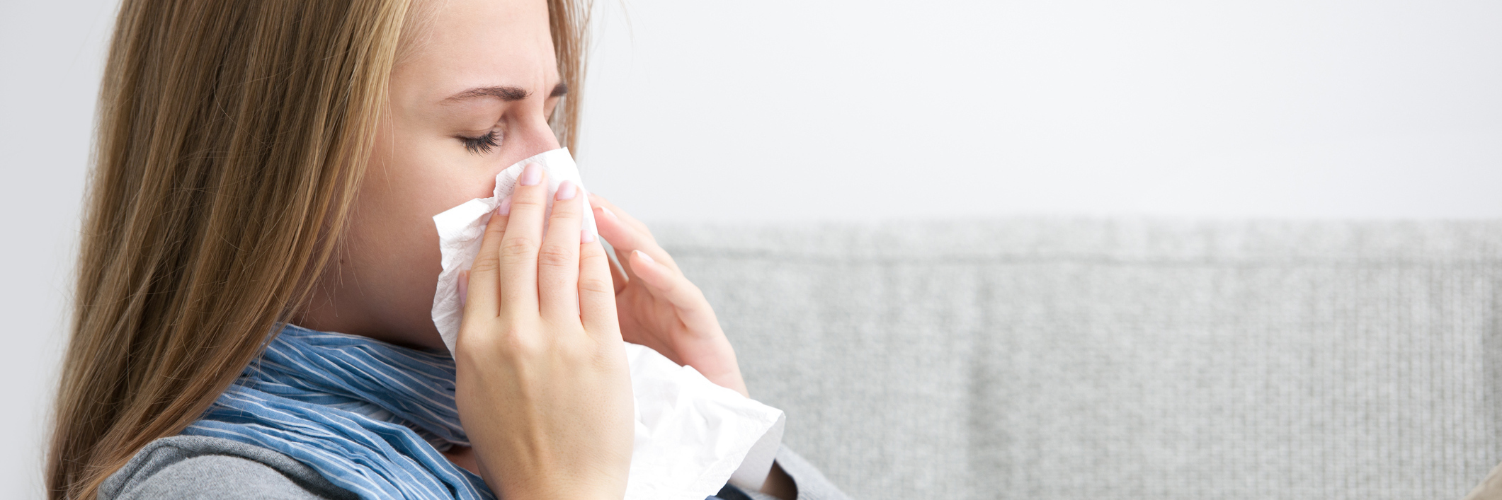Dangers of Always Getting Infections Due to Weak Immune System woman sitting on her couch and blowing her nose