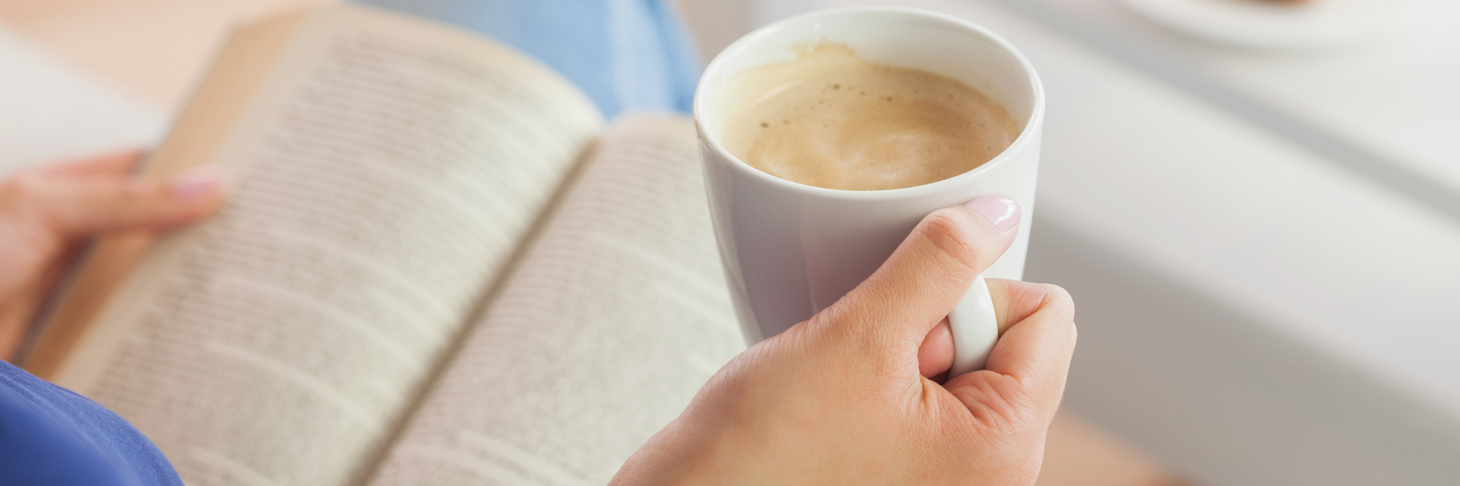Woman sitting on the sofa reading a book holding her coffee mug