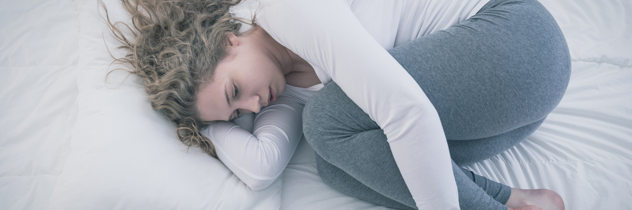 young woman curled up on bed looking depressed