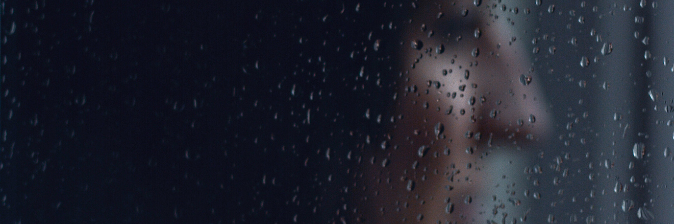 Image of woman's profile through window with rain drops on window