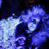 Focus on blue illuminated treebark, a girl with furry hood next to it