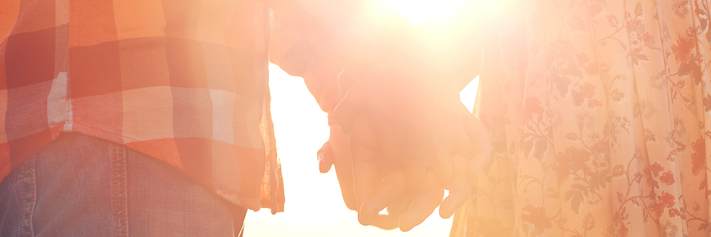 A couple holding hands, sunshine flowing through their arms.