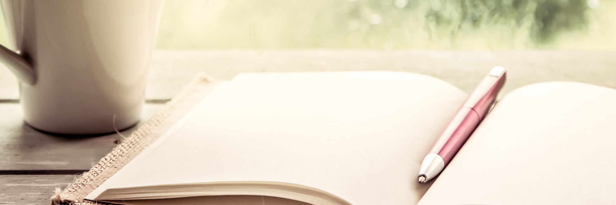 pen on an open notebook sitting next to a mug on a windowsill