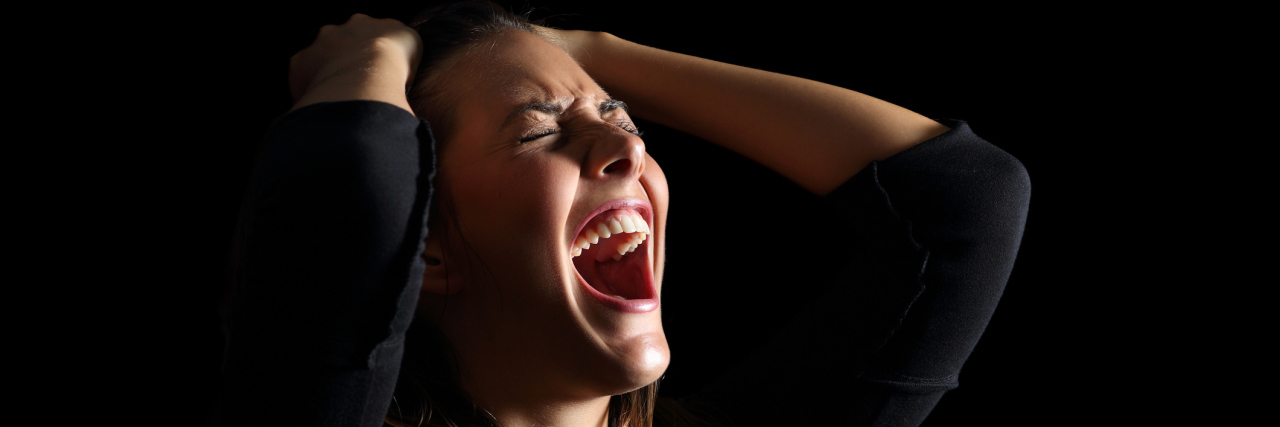 Depressed woman crying and shouting desperately isolated in a black background