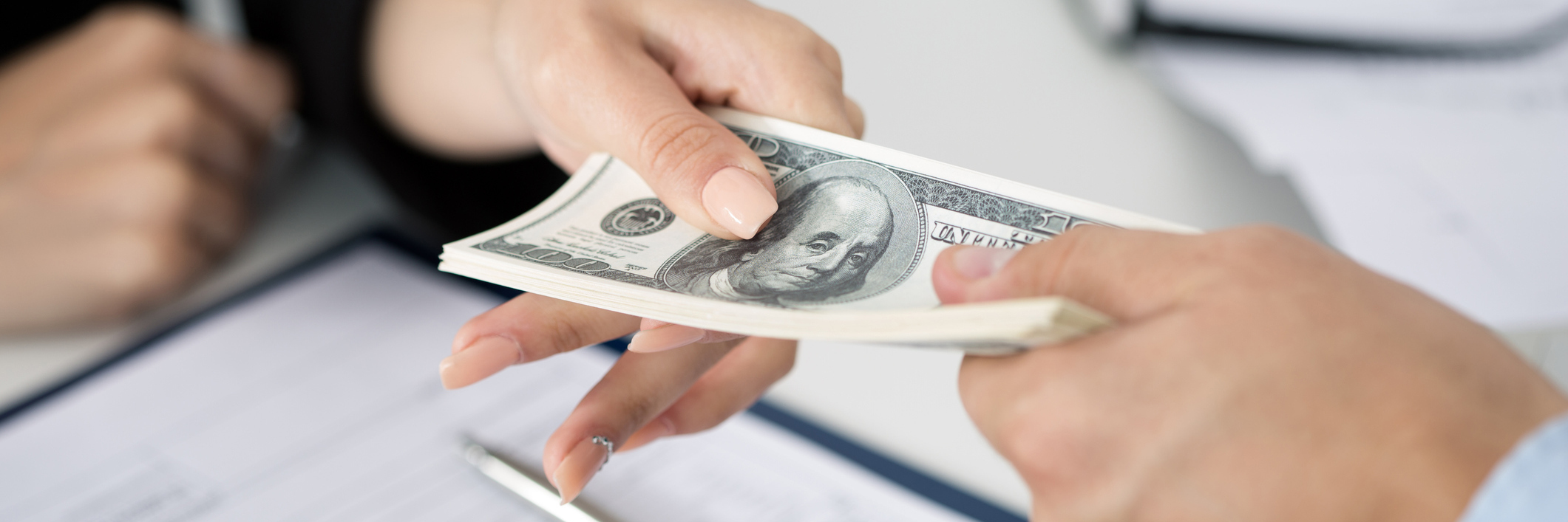 Ulcerative Colitis: The Financial Impact of Chronic Illness woman handing a stack of hundred dollar bills to receptionist