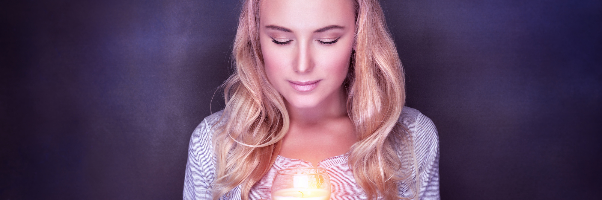 A woman in front of a dark background hodls a burning candle.