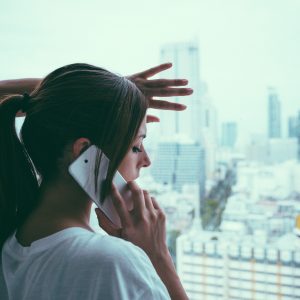 woman on phone standing at window looking out at gray sky