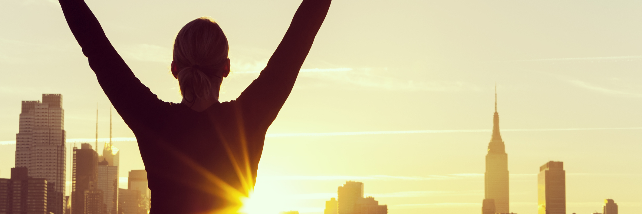 Focusing on the Positives in Life With Chronic Illness woman with her arms raised in success by the new york skyline at sunrise