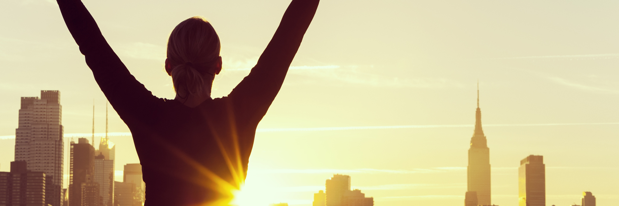 woman with her arms raised in success by the new york skyline at sunrise