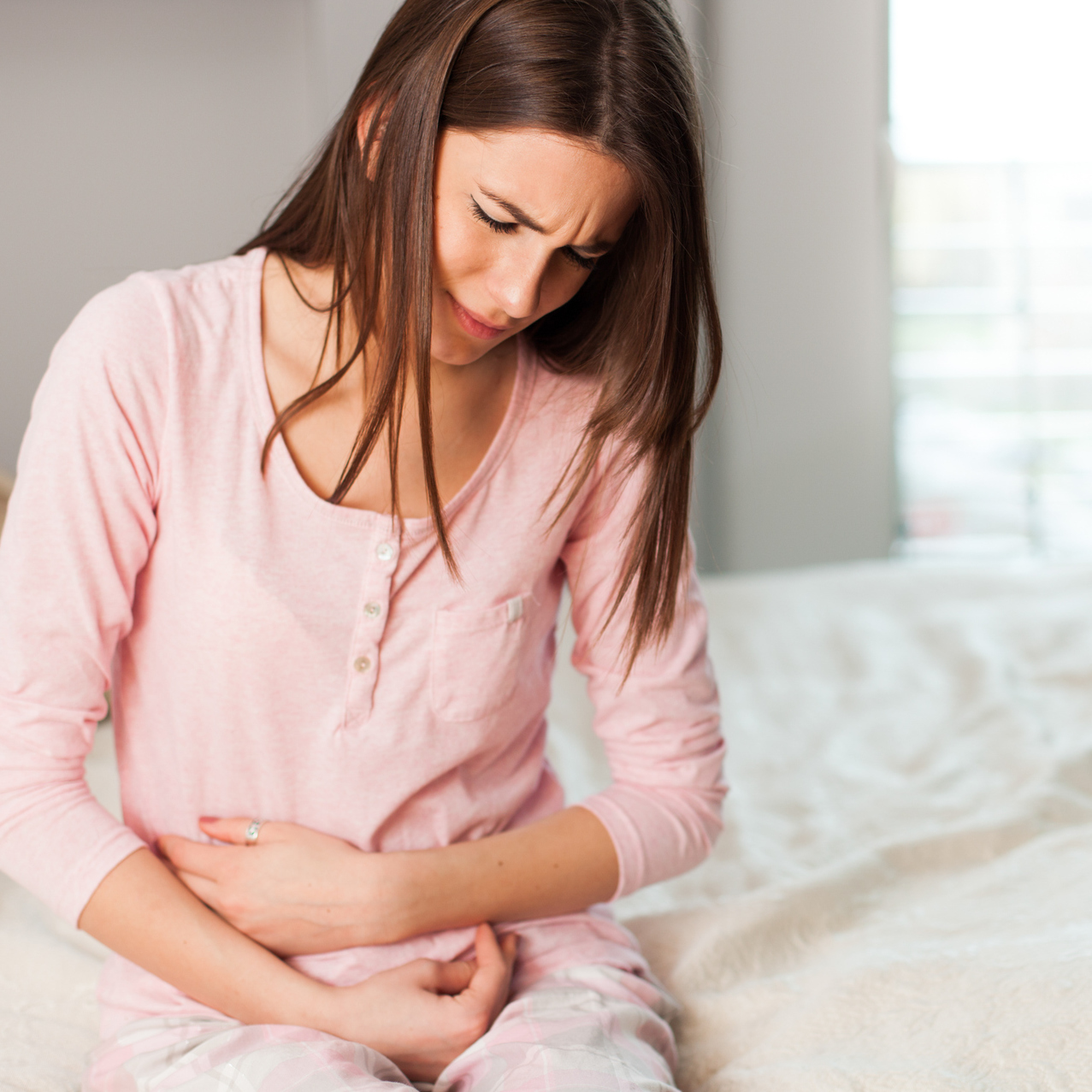 young woman sitting on bed with stomachache holding stomach