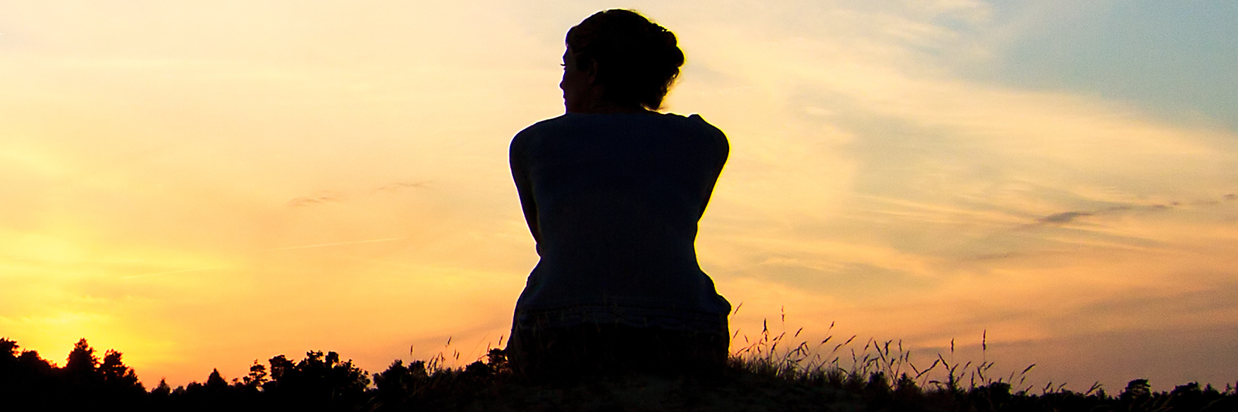 Silhouette of woman sitting on grass at sunset