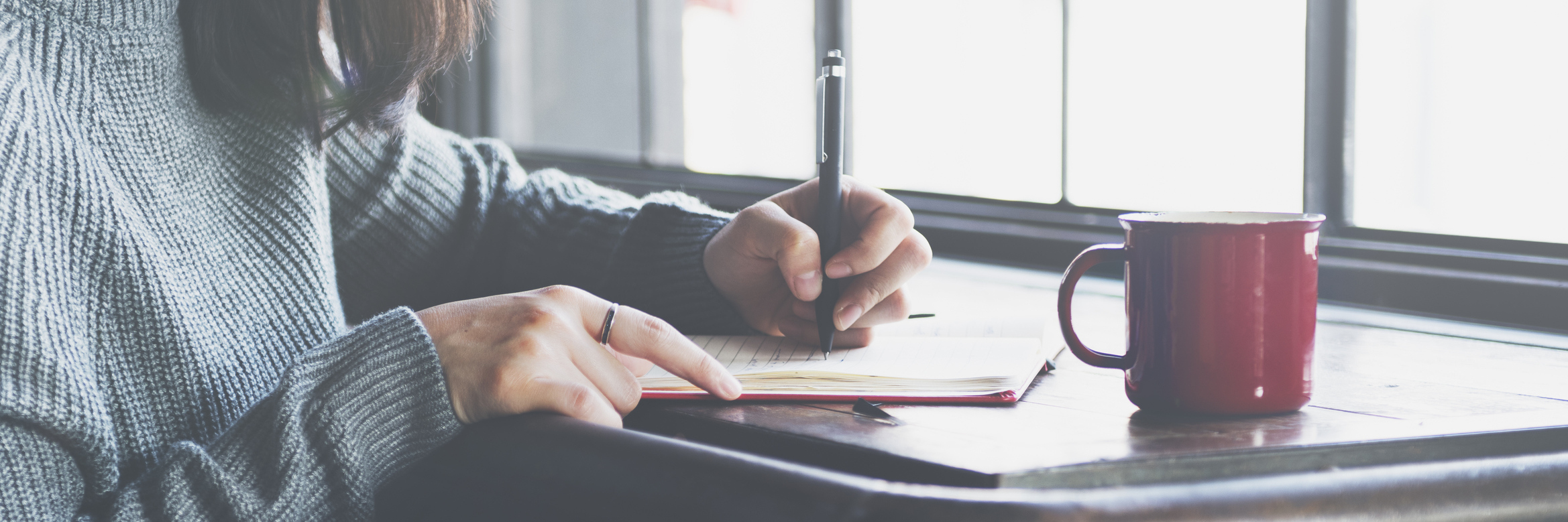 A woman writes in her journal, coffee mug a few inches away.