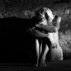 black and white photo of lonely woman in dark place hugging knees against rough wall