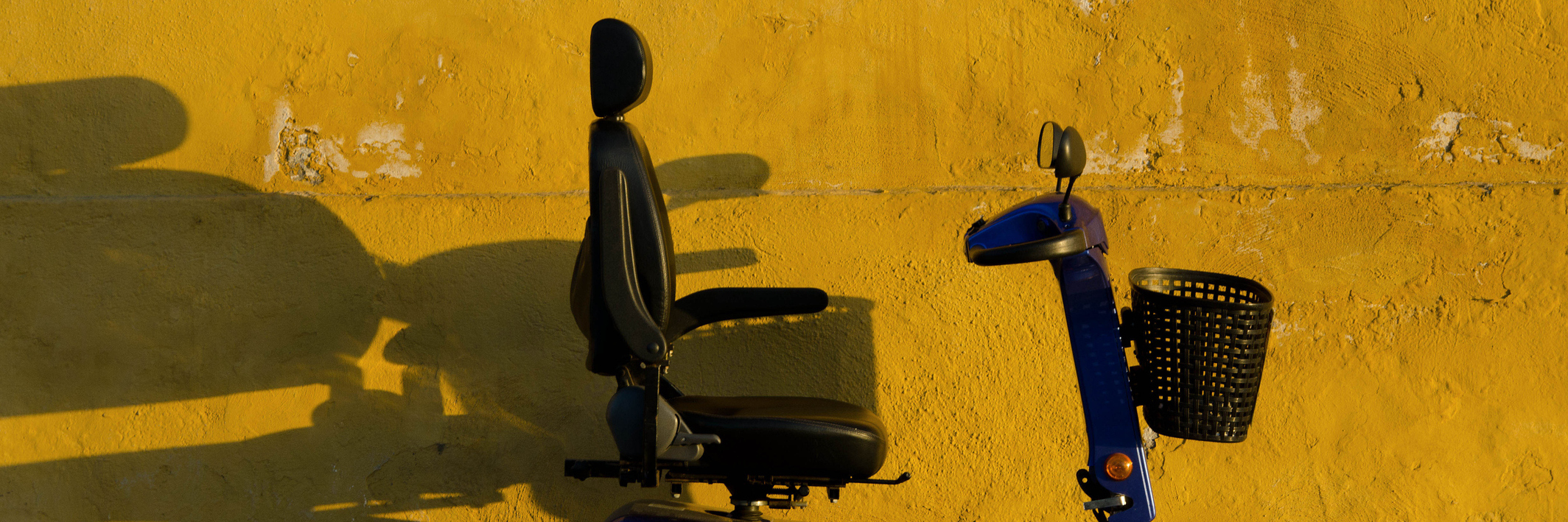 Blue scooter against yellow wall.
