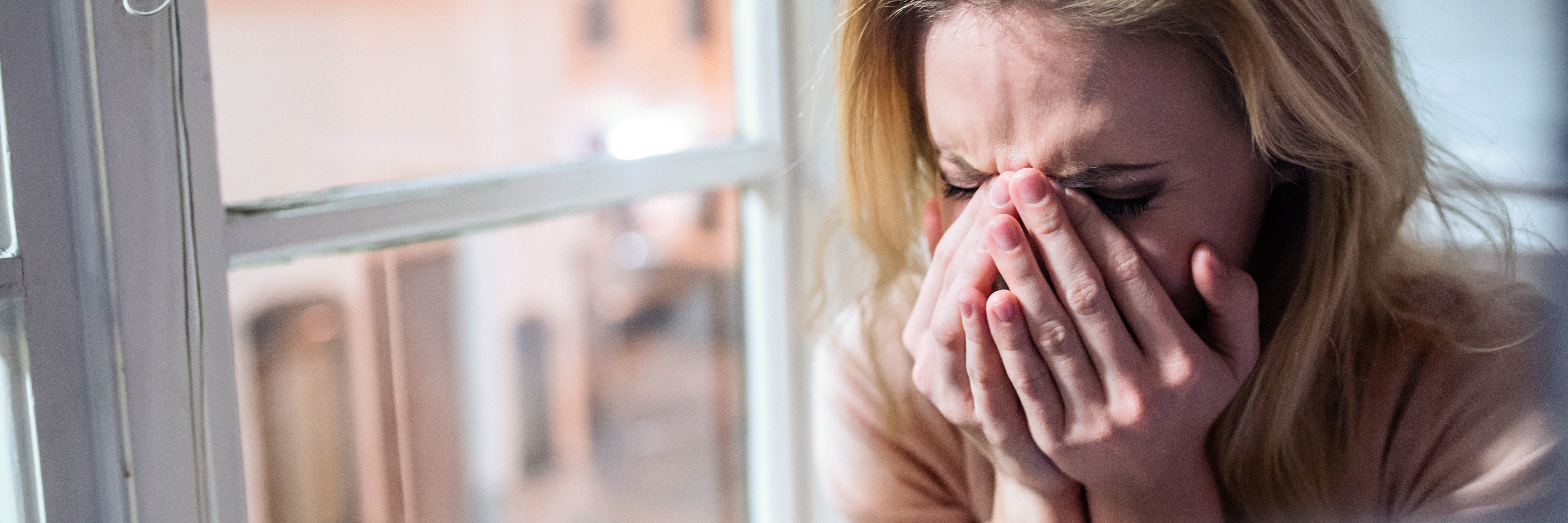 young blonde woman sitting by window crying