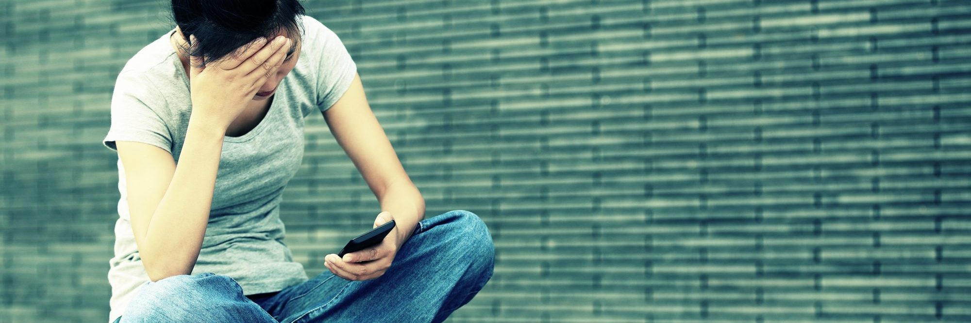 What My Anxiety Tells Me When I'm Waiting for a Message Reply young asian woman sitting cross legged in city with smartphone