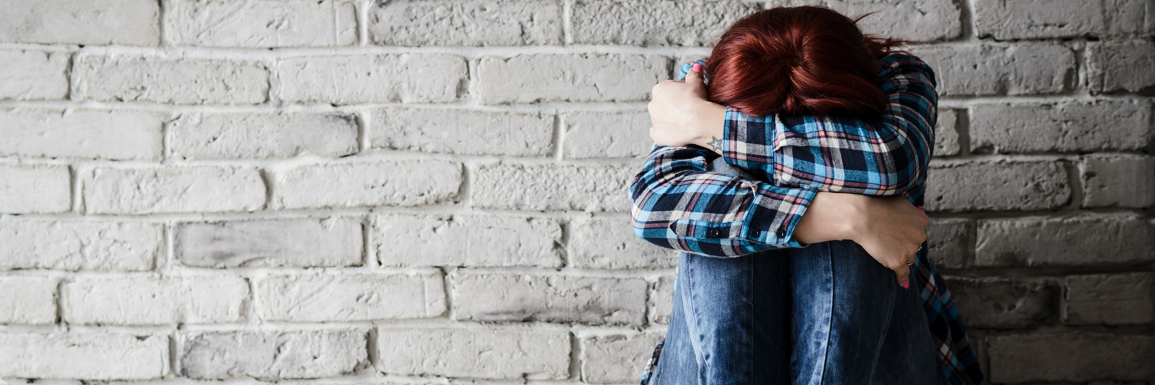 How I Recovered From a Major PTSD Breakdown young crying depressed woman with head buried in arms sitting against a brick wall