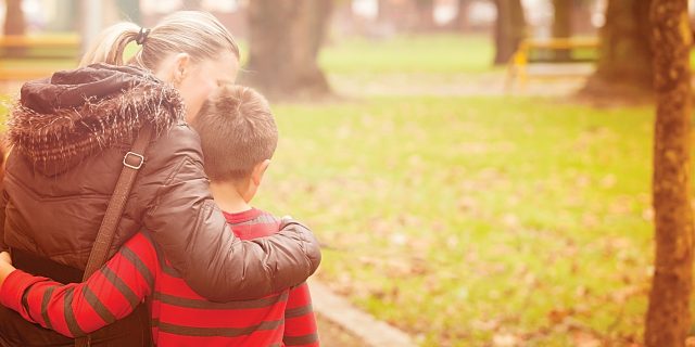 woman hugging son and walking in park