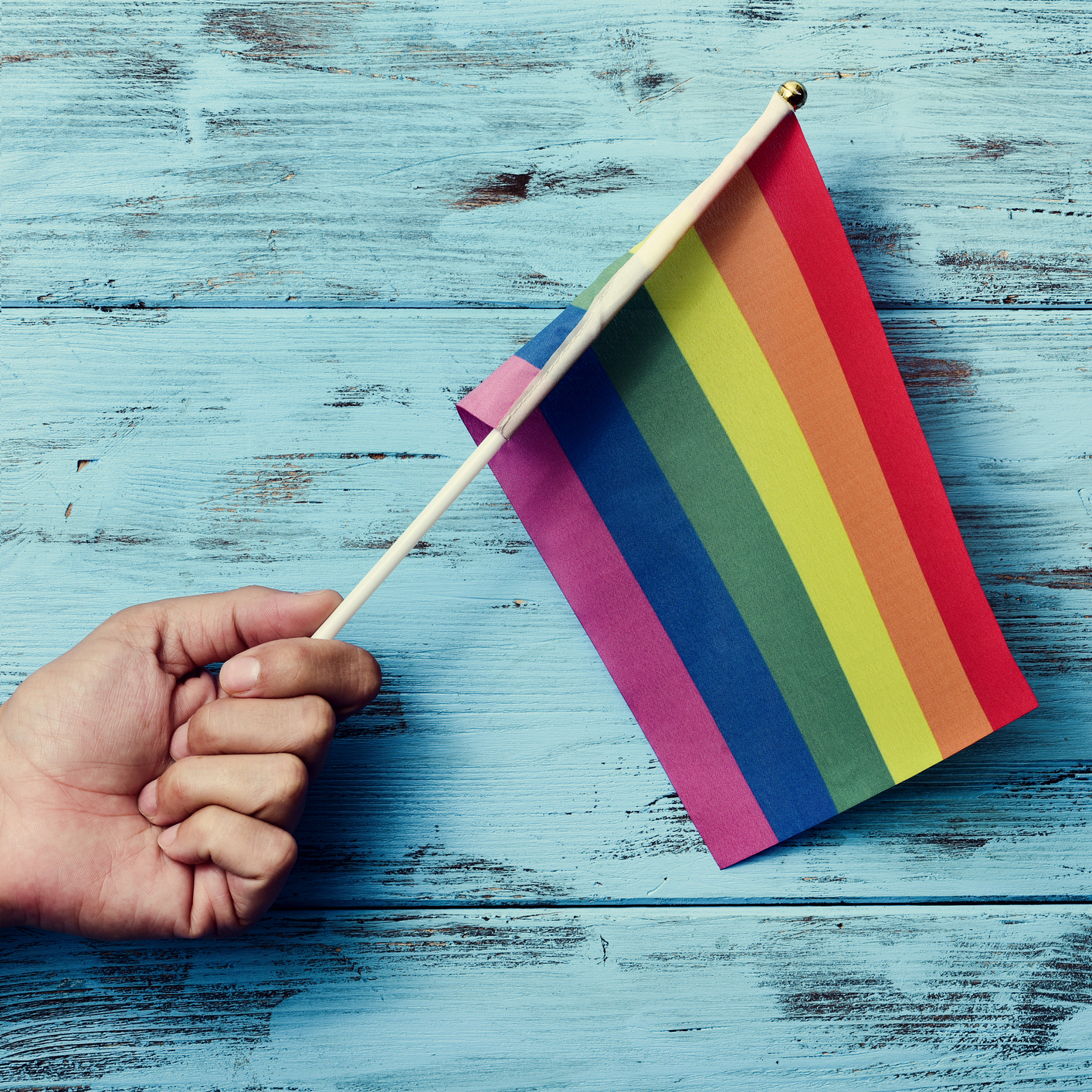 Someone holding a rainbow flag against a blue background.