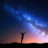 Illustration of colorful night sky with Milky Way pictured and a silhouette of a woman standing underneath it with arms raised