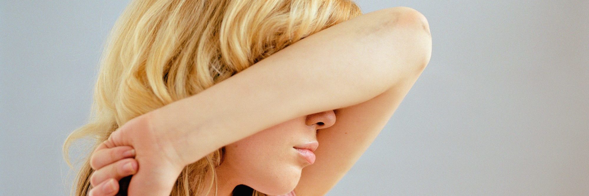 blonde woman covering face with arm