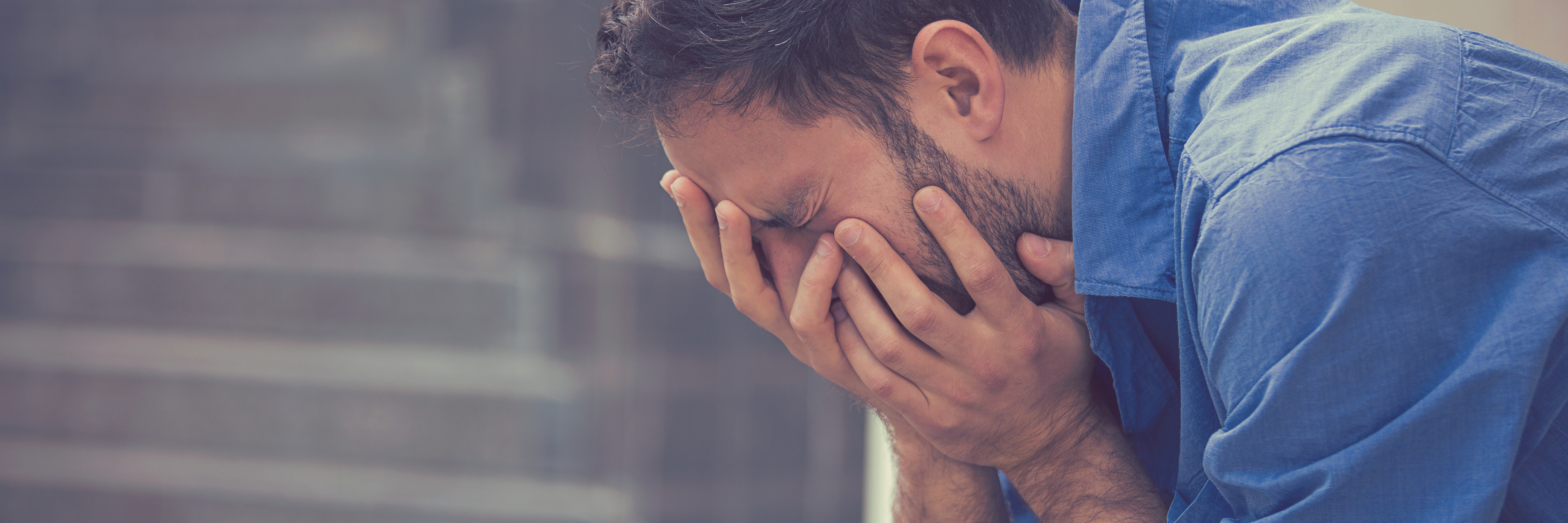 man sitting outside crying with head in hands