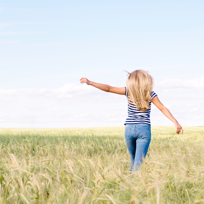 young blonde woman with arms outstretched in field