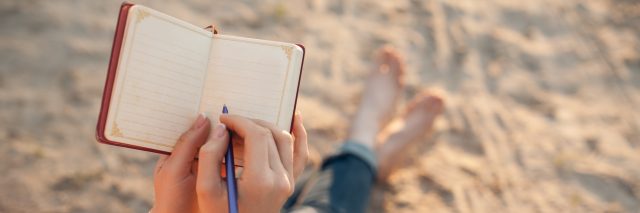 Young woman sitting on the beach writing.