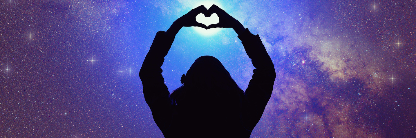 Silhouette of woman making heart shape with hands, with arms extended toward starry night sky